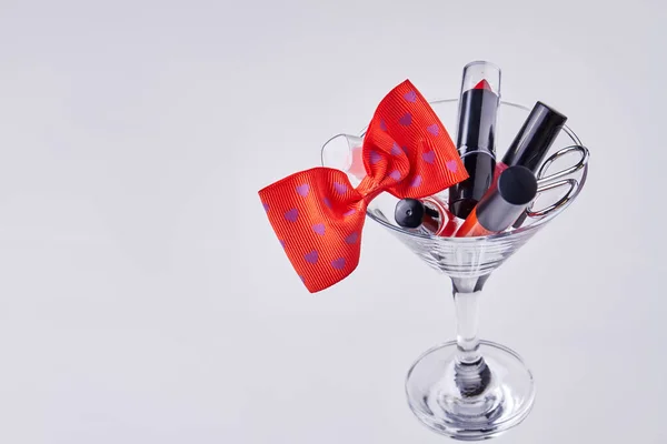Makeup accessories and red bow tie in a cocktail glass. Isolated on white background.