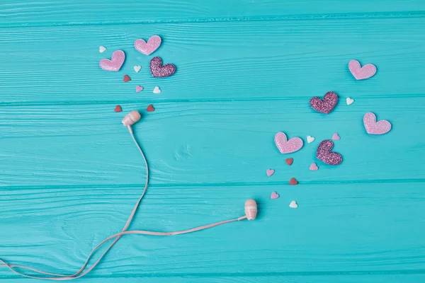 Earphones with pink and purple hearts on blue wood. Love for music concept.