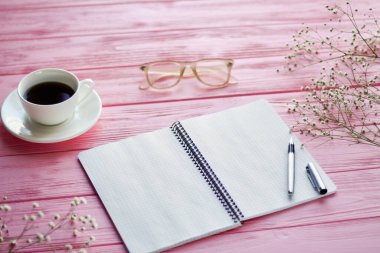 Top view blank notepad with coffee cup and glasses. Pink wooden desk.