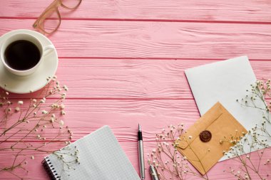 Top view flat lay office accessories and copy space on pink wood. Coffee cup with notepad and envelope.