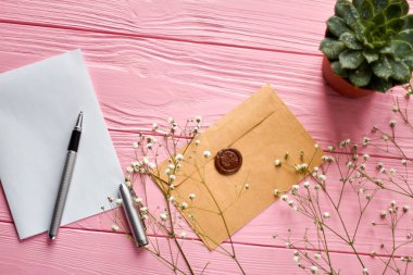 Top view envelope with seal and blank paper. Pink wooden desk background.