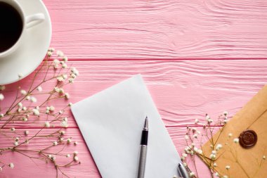 Top view blank notepad with pen and coffee cup. Pink wooden desk with copy space.