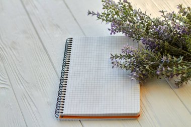 Blank notepad and purple flowers on wooden desk. Checkered page for copy space.