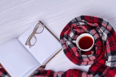Top view cup of tea with scarf. Blank notebook with glasses.