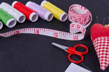 Close up set of sewing accessories on dark surface. Threads with measure tape and scissors.