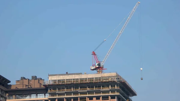 建物の上にブロックを運ぶ建設クレーン 青空の背景 — ストック写真