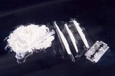 Pile of white powder drugs and glass smoking pipe. Razor and cocaine lines for snorting.