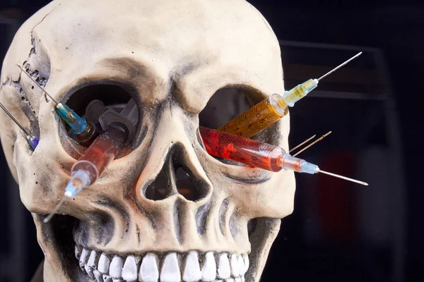Humans skull with syringes filled with colorful liquid. Danger of drugs concept. Isolated on black background.