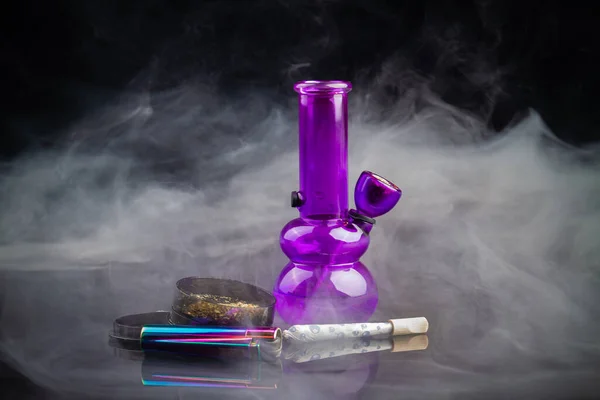 Purple glass bong pipe with joint and a lot of smoke. Cannabis smoker starter pack.