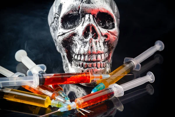 Humans skull with pile of syringes with a lot of smoke. Pile of syringes with pile drug liquid.