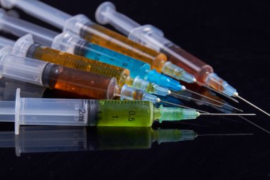 Close-up pile of syringes with colored drugs for injection. Isolated on black background.