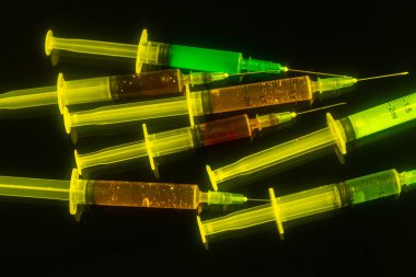 Many syringes with yellow lighting isolated on black background. Drug dependence addiction concept.