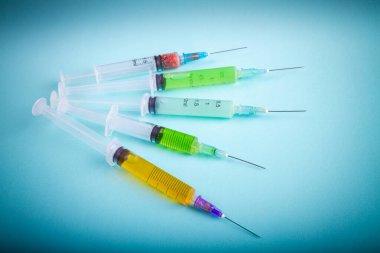 Several various syringes with multicolored medicine on blue background. Drugs or vaccine injections.