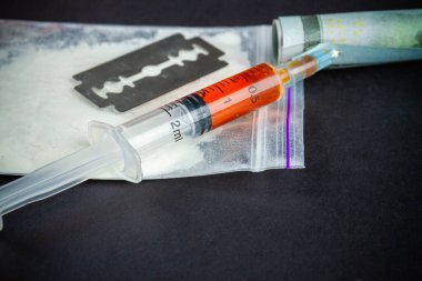 Close-up syringe filled with drug with razor and pack of cocaine. Drug dependence addiction concept.