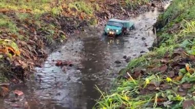 Flatbed towing truck toy going along forest puddle. RC vehicle moving on the water after heavy rain.