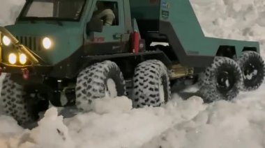 Remote control toy truck going on the snow. RC flatbed towing truck with glowing headlights.
