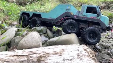 Flatbed towing truck with wet wheels overrides big rocks. Rough terrain countryside race in a forest after rain.
