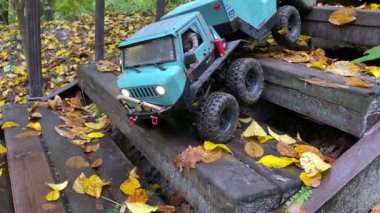 RC flatbed towing truck going downstairs in autumn park. Radio control toy vehicle on wet wooden stairs after rain.