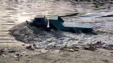 RC vehicle moving on pond shore sand and shallow water. Radio controlled flatbed towing truck.