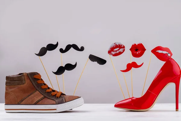 Mens and womens shoes on white background. Red High heel shoes with lips. Brown sneakers with moustache.