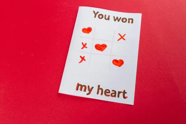 Paper with you won my heart inscription. Tic tac toe. Romantic love declaration on red background.