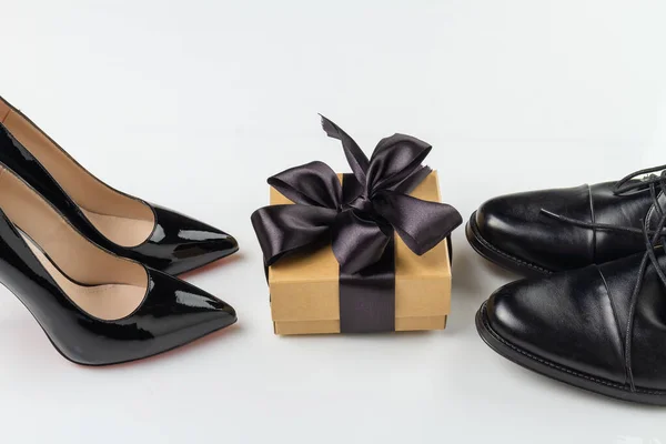 Black mens and womens shoes and a gift box with a ribbon. Fashionable and stylish accessories. Sale and delivery of shoes concept.