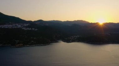 Dağlı güzel deniz manzarası ve turuncu gün batımı gökyüzü. Akşamları tatil köyünün panoraması. Resimli doğa manzarası.