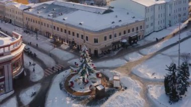 Karlı şehir meydanında havadan görünüşlü bir atlıkarınca. Kaldırımlar ve çatılar karla kaplı..