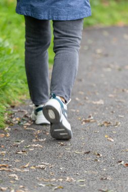 Düşen yapraklarla kaplı asfalt yolda yürüyen genç bir adamın bacakları.