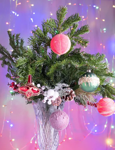 水晶花瓶中的枞树枝头装饰着圣诞或新年庆祝活动，背景上点缀着仙灯. — 图库照片