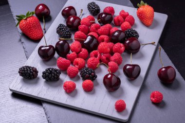 Gri taş tahtada kiraz, ahududu ve böğürtlen.