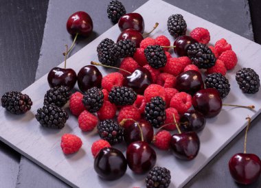 Gri taş tahtada kiraz, ahududu ve böğürtlen.