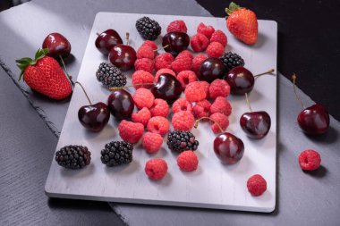 Gri taş tahtada kiraz, ahududu ve böğürtlen.