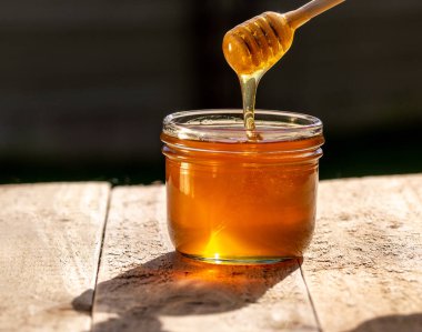 Bal kavanozu ahşap masada ve kara sırtüstü, bal damlatan bal.