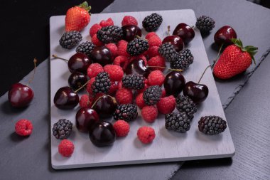 Gri taş tahtada kiraz, ahududu ve böğürtlen.