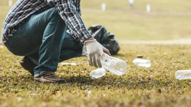 A man is picking up trash in a park, not throwing trash in the trash can ruin the beauty of the garden area and also cause global warming and harm animals. Concept of cleanliness in public areas.