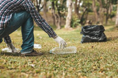 A man is picking up trash in a park, not throwing trash in the trash can ruin the beauty of the garden area and also cause global warming and harm animals. Concept of cleanliness in public areas.