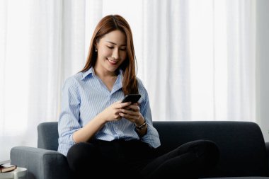 Oturma odasındaki kanepede akıllı telefon oynayan bir kadın, yoğun bir iş gününden sonra hafta sonları dinleniyor, internetten alışveriş yapıyor ve kredi kartıyla ödüyor. Kredi kartı ödeme kavramı.