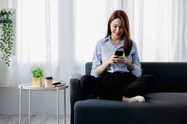 Oturma odasındaki kanepede akıllı telefon oynayan bir kadın, yoğun bir iş gününden sonra hafta sonları dinleniyor, internetten alışveriş yapıyor ve kredi kartıyla ödüyor. Kredi kartı ödeme kavramı.