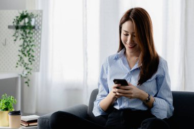 Oturma odasındaki kanepede akıllı telefon oynayan bir kadın, yoğun bir iş gününden sonra hafta sonları dinleniyor, internetten alışveriş yapıyor ve kredi kartıyla ödüyor. Kredi kartı ödeme kavramı.