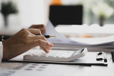 Bir şirketin mali belgelerindeki rakamları hesaplamak için hesap makinesi kullanan bir işadamı, şirketin nasıl büyüyeceğini planlamak için tarihsel finansal verileri analiz ediyor. Mali konsept.