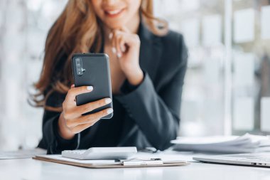 Young businesswoman looking at financial information from a mobile phone, she is checking company financial documents, she is a female executive of a startup company. Concept of financial management.