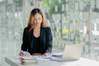 A beautiful Asian businesswoman sitting in her private office, she is checking company financial documents, she is a female executive of a startup company. Concept of financial management.