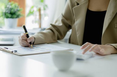 Bir şirketin mali belgelerindeki rakamları hesaplamak için hesap makinesi kullanan bir işadamı, şirketin nasıl büyüyeceğini planlamak için tarihsel finansal verileri analiz ediyor. Mali konsept.