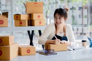 Bir e-ticaret şirketini işleten kadın, onlara göndermeden önce müşterilerin bir listesini kağıda yazıyor. Web sitelerinde ve sosyal medyada bir e-ticaret şirketi işletiyor. Çevrimiçi ürün satma kavramı.