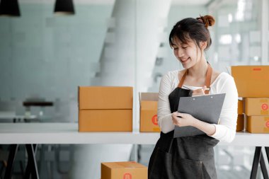 Bir çevrimiçi mağazanın sahibi, paketlenmiş ürünlerin siparişlerini web sitesinden sipariş edildiği gibi müşterilere teslimata hazırlamak için kontrol etmektedir. Çevrimiçi satış ve online alışveriş kavramları.