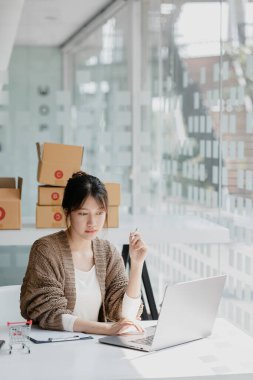 Güzel bir Asyalı işletme sahibi online bir dükkan açıyor, müşterilerin siparişlerini dizüstü bilgisayarla kontrol ediyor, malları bir kurye şirketi aracılığıyla gönderiyor, bir kadının online iş kurma kavramı.