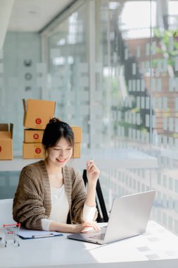 Güzel bir Asyalı işletme sahibi online bir dükkan açıyor, müşterilerin siparişlerini dizüstü bilgisayarla kontrol ediyor, malları bir kurye şirketi aracılığıyla gönderiyor, bir kadının online iş kurma kavramı.