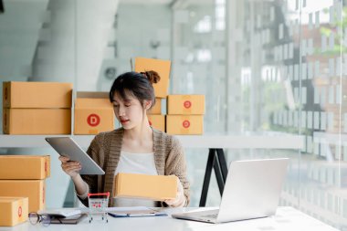 Güzel bir Asyalı işletme sahibi online bir dükkan açıyor, müşterilerin siparişlerini kontrol ediyor, bir kurye şirketi aracılığıyla mal gönderiyor, bir kadının online iş kurma kavramı.
