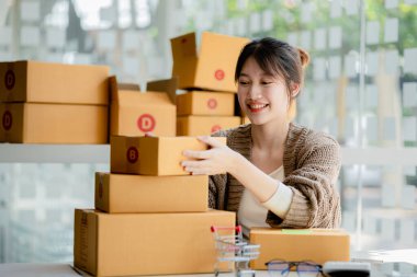 Güzel bir Asyalı işletme sahibi online bir dükkan açıyor, müşterilerin siparişlerini kontrol ediyor, bir kurye şirketi aracılığıyla mal gönderiyor, bir kadının online iş kurma kavramı.